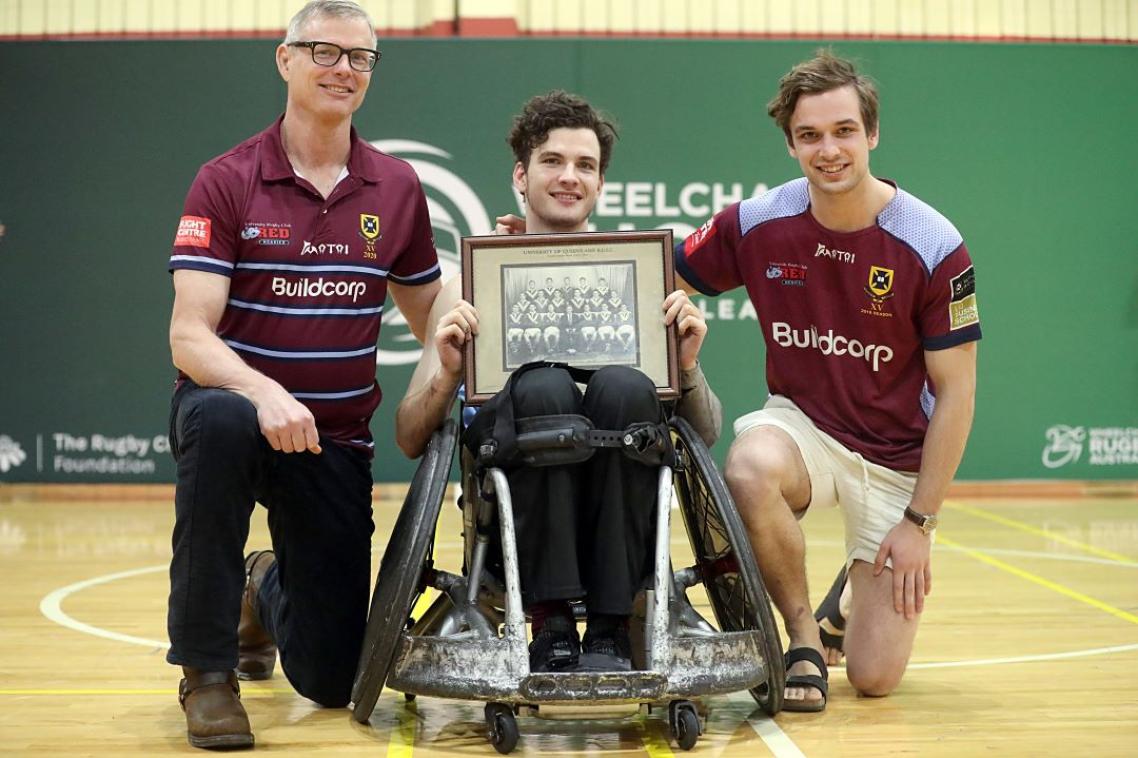 Two men sitting next to a younger man in a wheelchair, holding a framed photo