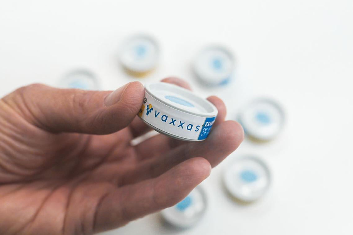 A hand holding a cannister containing the vaccine patch.