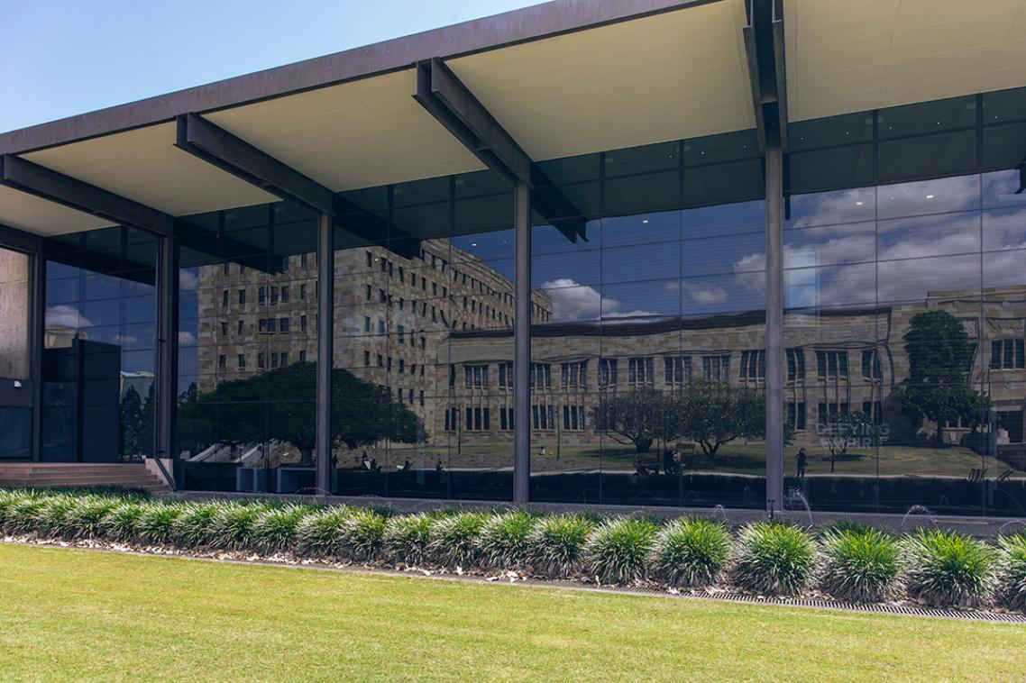 Sandstone building reflected onto glass windows, grass in the foreground