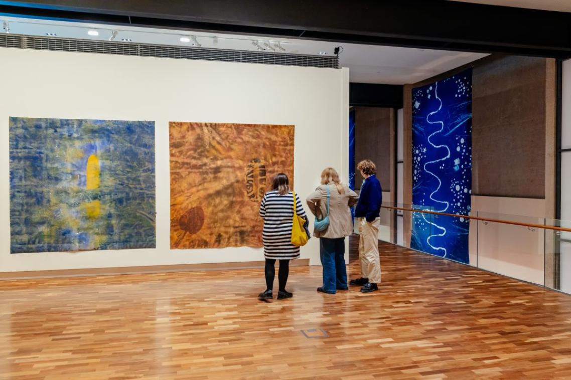 Three people standing in a gallery looking at paintings