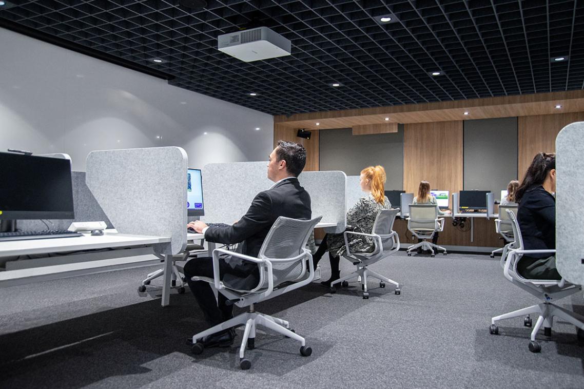 A computer lab of people sitting on wheelie chairs.