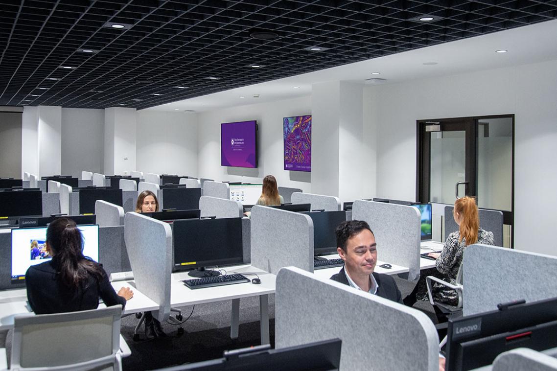 A computer lab of people sitting on wheelie chairs.