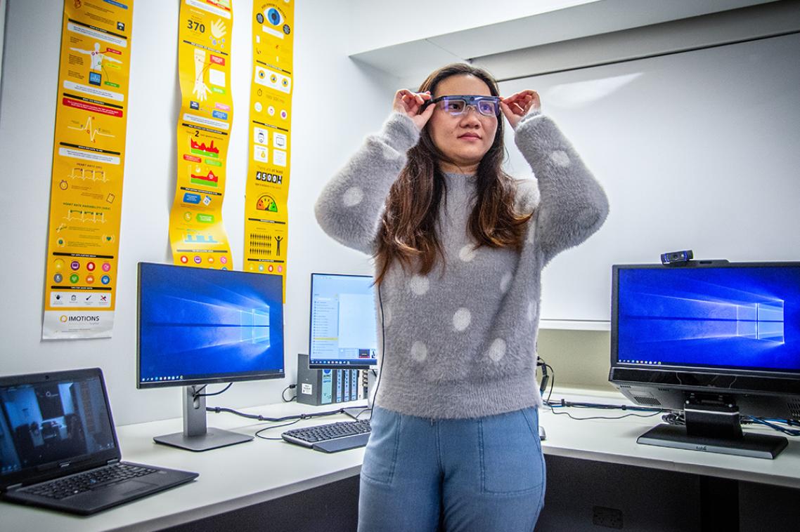 a woman in a grey sweater wearing glasses in a computer lab.