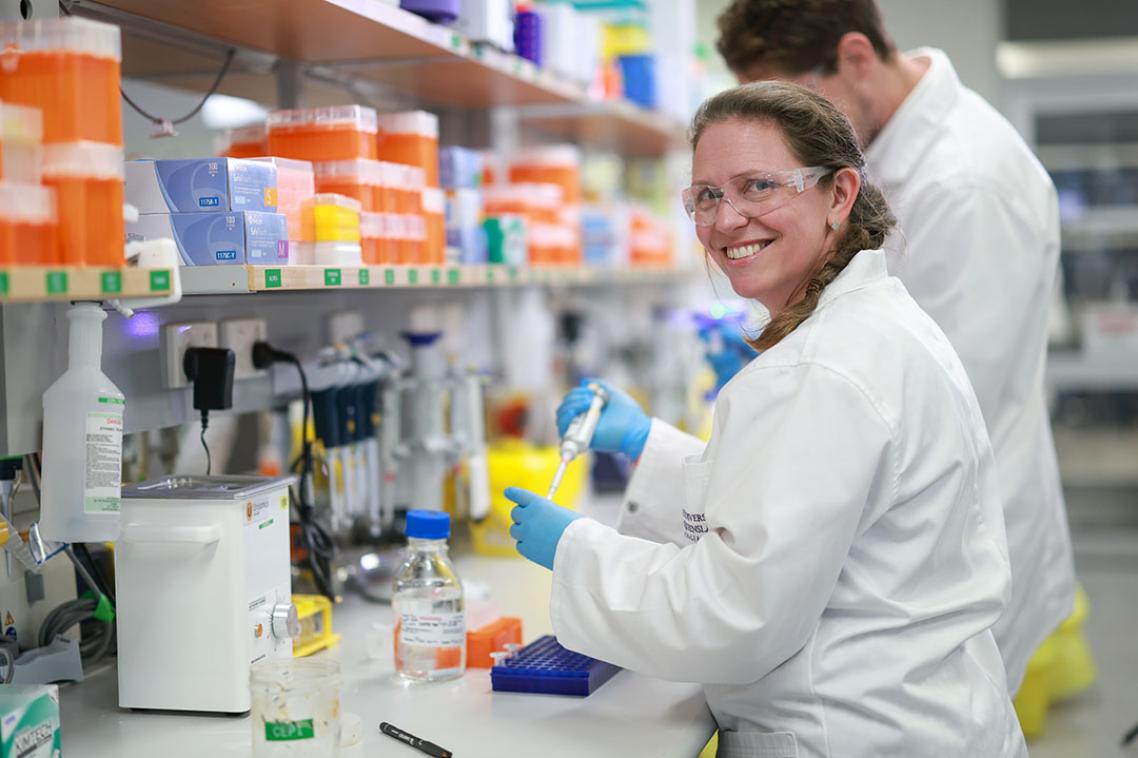 A male and female researcher in a lab coat standing at a lab bench