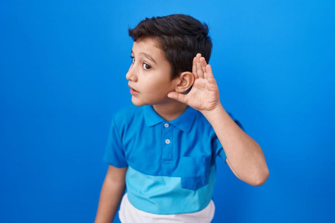 Young boy cupping his left hand to his left ear.