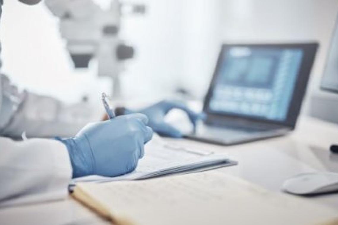 A closeup of gloved hands writing notes in front of a laptop
