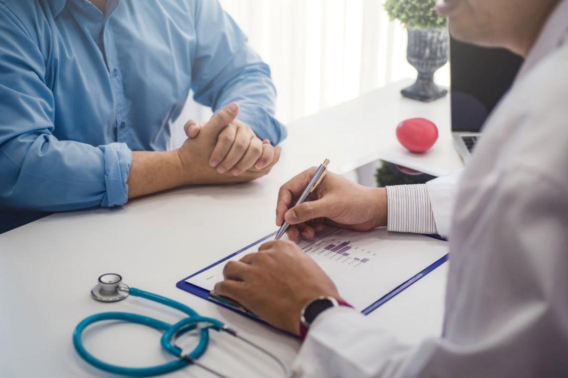 A man sitting across from a doctor with a stethescope and clipboard on the table