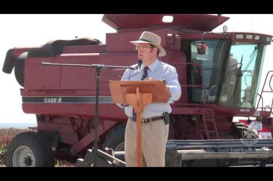 A man delivers an address from a lectern in front of a combine harvester