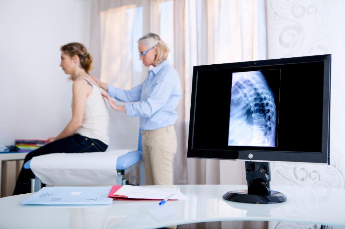 Health professional examining spine of female patient with x-ray in foreground. Adobe