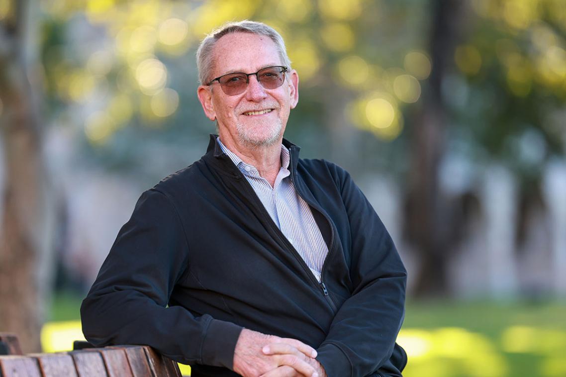 A man in dark sunglasses and a suit sitting on a park bench