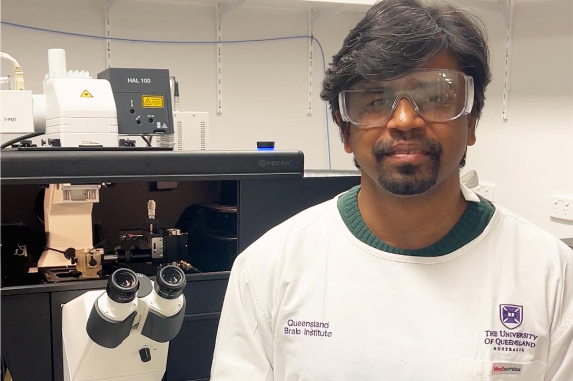 A man in a lab coat and protective goggles standing in front of a microscope