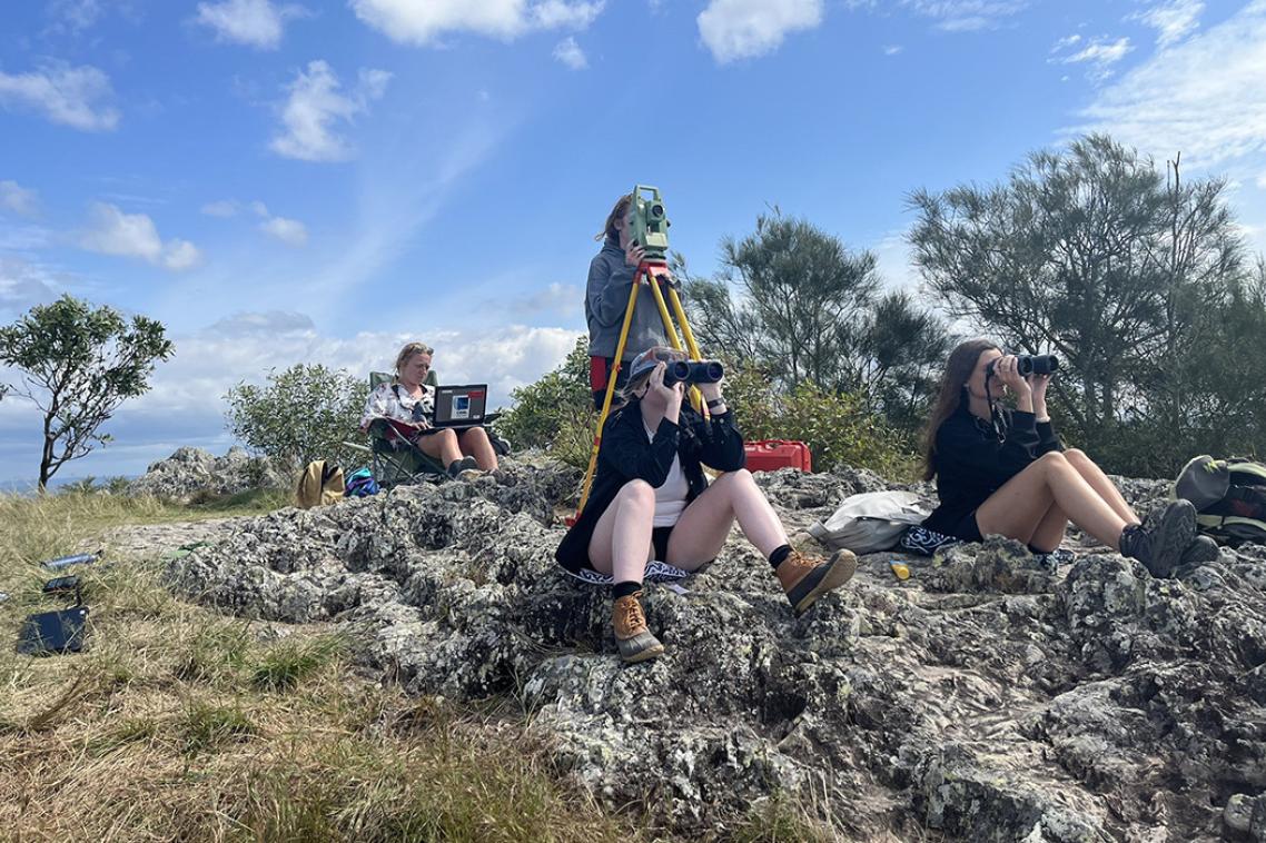 a group of people sit on rocks with binoculars