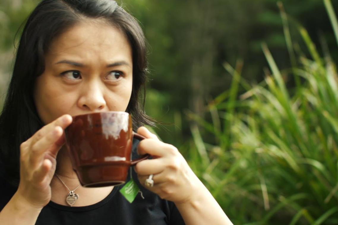 UQ graduate Maggie James drinks a cup of tea outside surrounded by plants