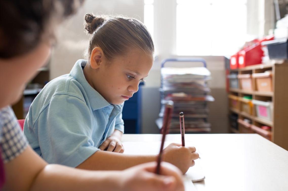 A young female Indigenous school student sitting at a desk writing.