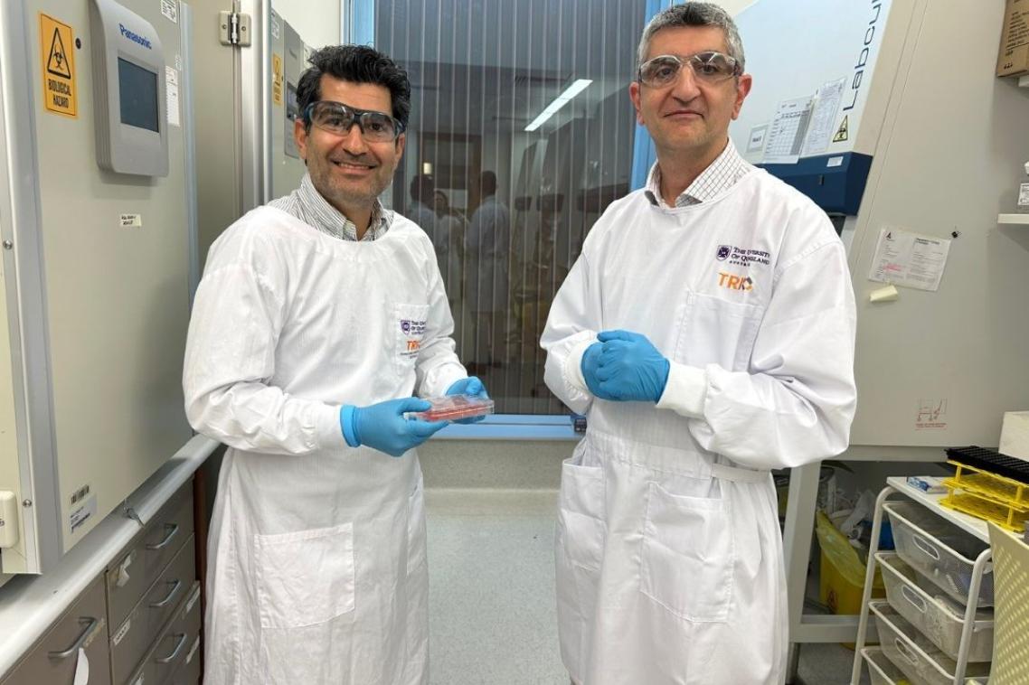 Two male scientists wearing white coats standing in a laboratory and one is holding a petrie dish.