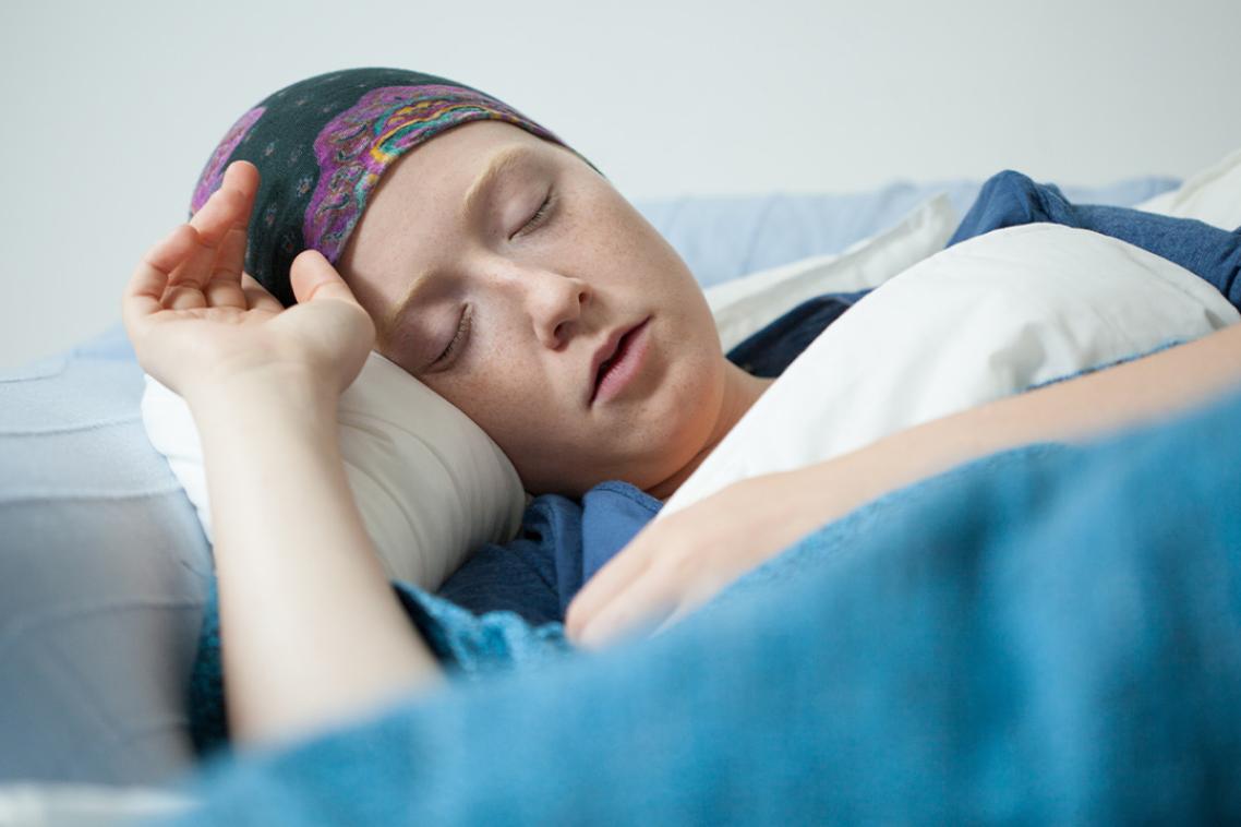 A young female patient in a headscarf lies with her eyes closed.