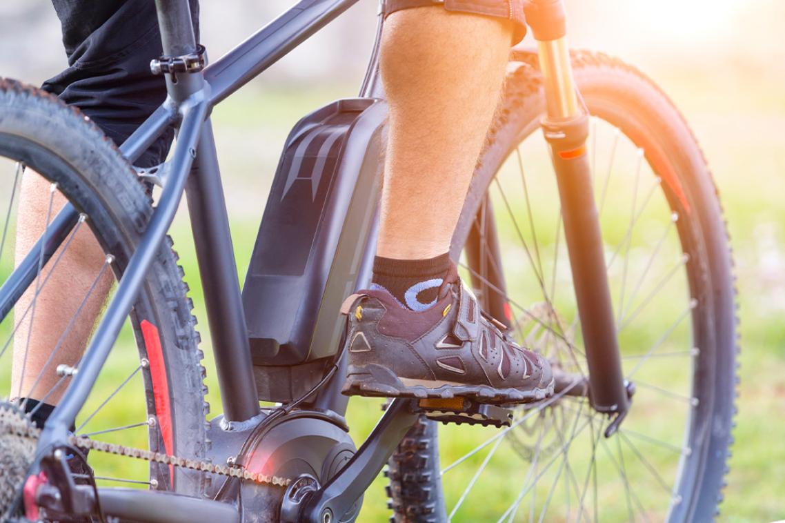 The pedals of an e-bike with a person's feet in trainers ready to ride.
