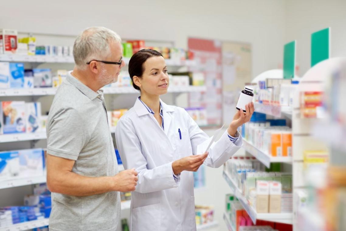 A pharmacist consulting a man on his medication, holding a script in one hand and a bottle in the other