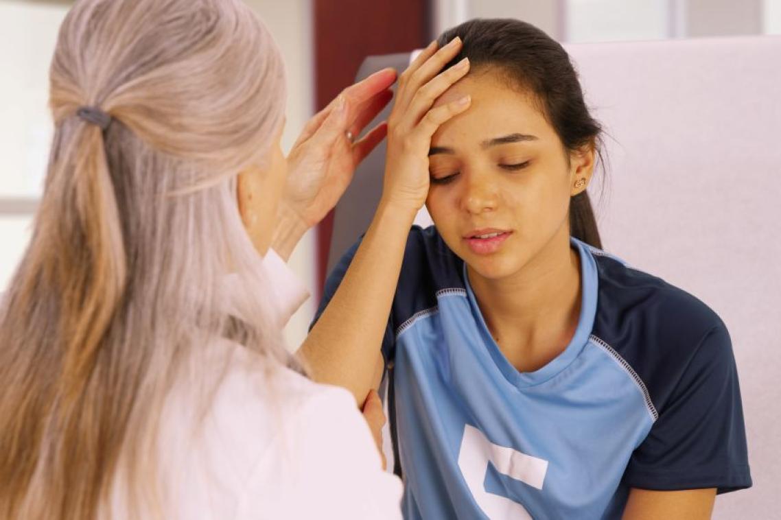A young soccer player with a head injury recieves medical attention. An elderly doctor checks the young soccer player for a concussion