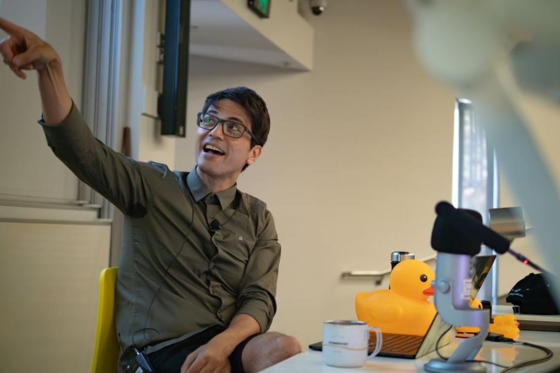 A man sitting at a desk pointing at a powerpoint slide on a projection