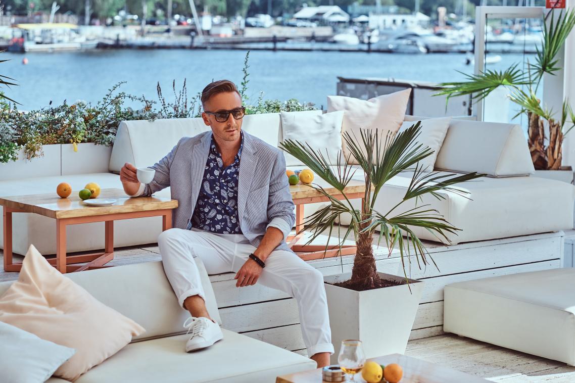 A wealthy looking man sits on a white couch near a harbour