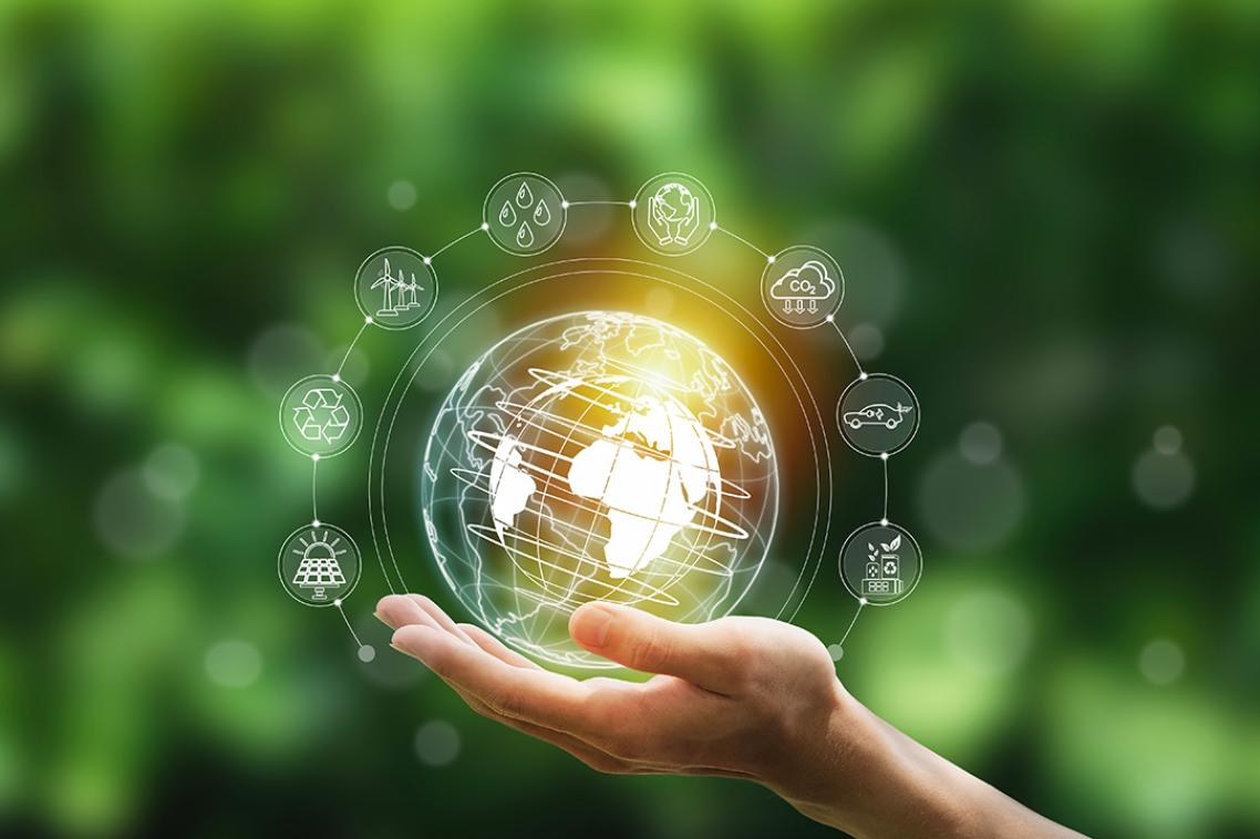 A hand holding a graphic of a globe surrounded by symbols of sustainability.