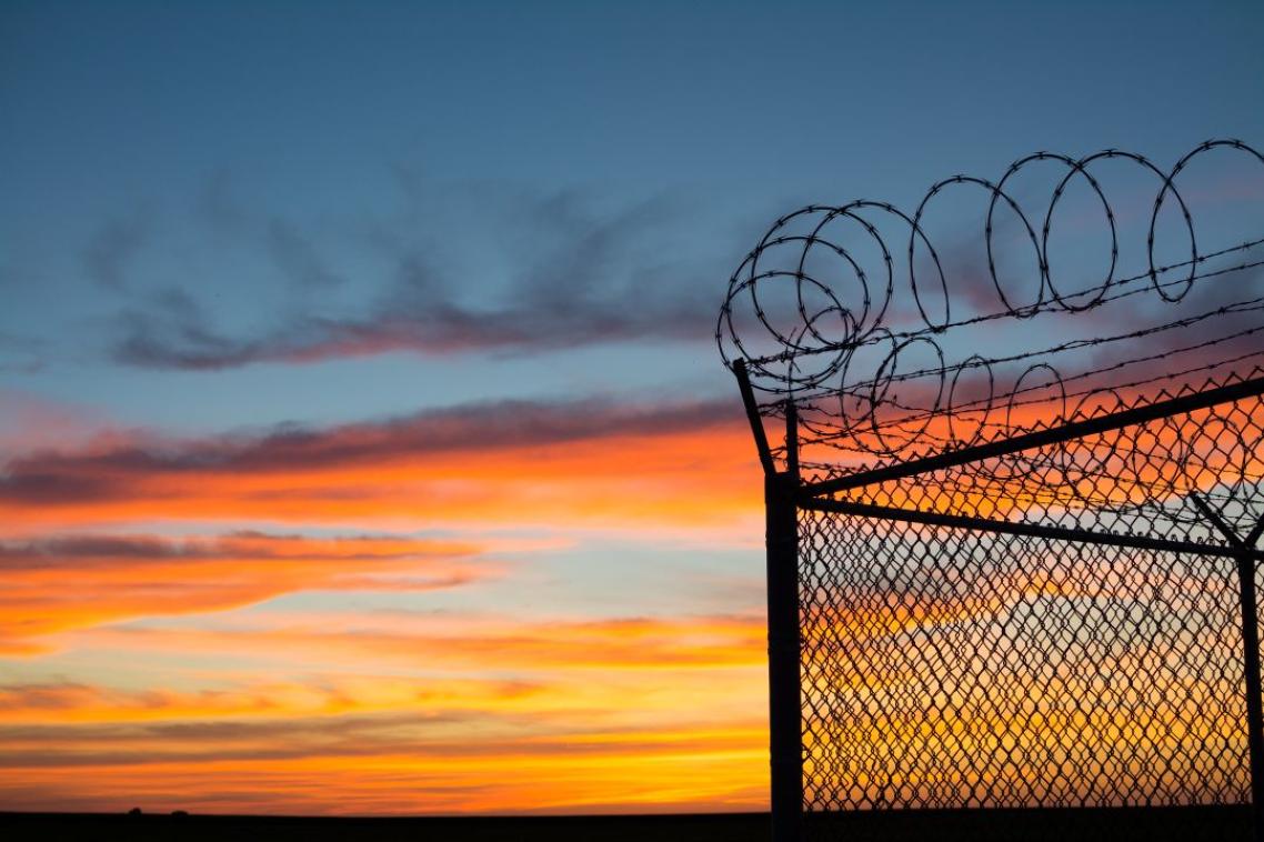 The sun sets behind a fence topped with razor wire