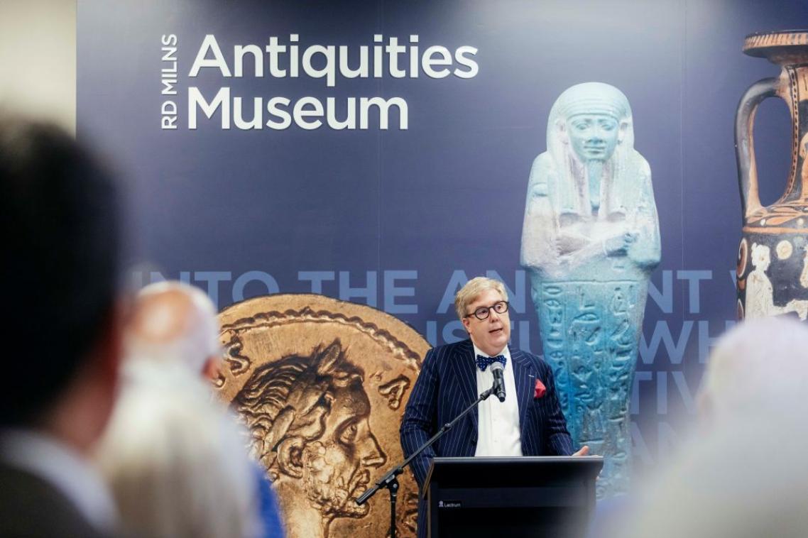 A in a navy striped tuxedo standing at a lectern addressing a crowd
