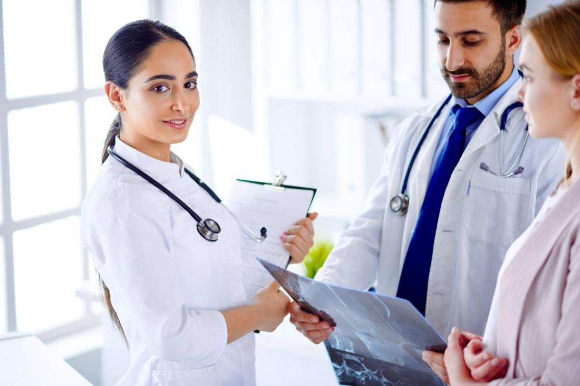 Two doctors communicate with a patient and show an x-ray to a patient in a hospital (female doctor looking at camera)