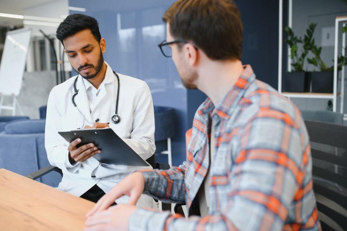 Male indian doctor giving prescription to male patient at clinic