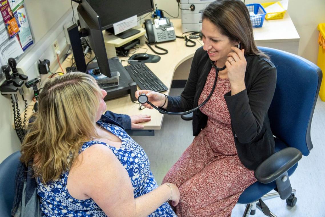 Female doctor taking blood pressure of female patient in clinic.