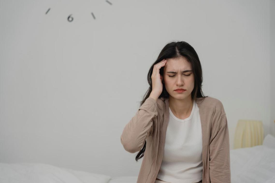 Young woman sitting on sofa holding her head in pain, showing signs of headache