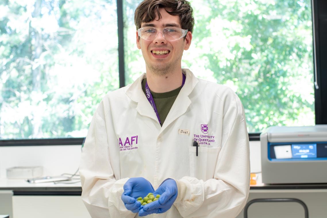 A man standing in a laboratory wearing a white coat and holding little green berries in blue gloves.