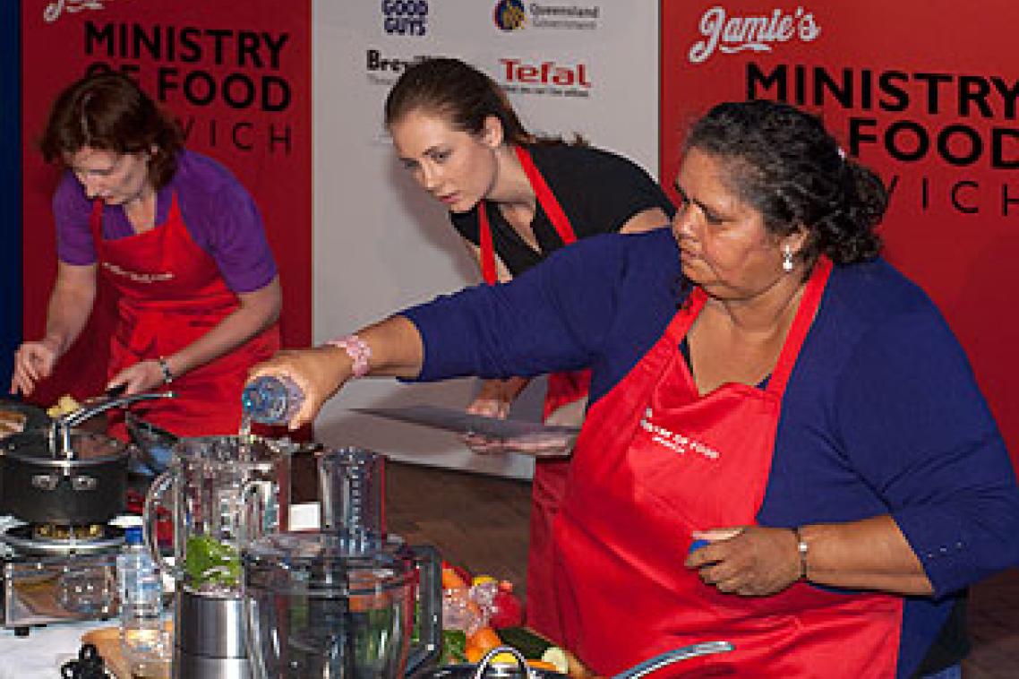 UQ student Charlotte Rashleigh assists Narrella Simpson, with Minister for Transport Rachel Nolan cooking in the background