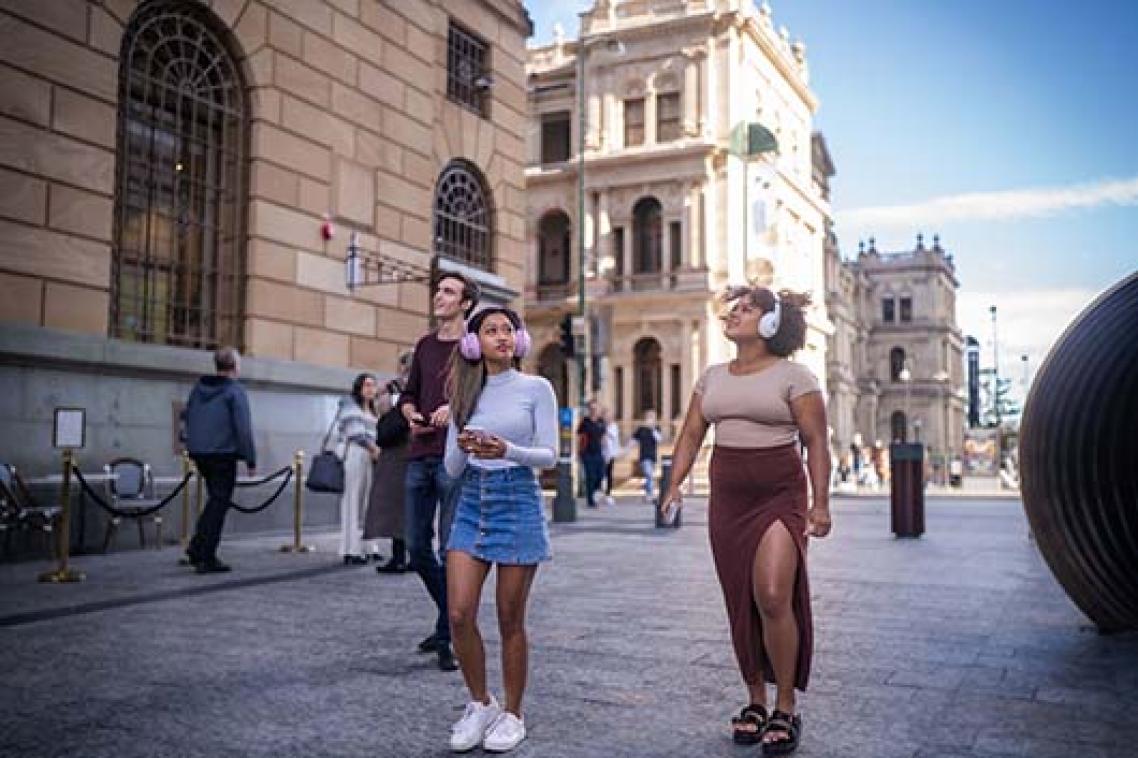 Three people standing in the middle of a city wearing headphones and looking up
