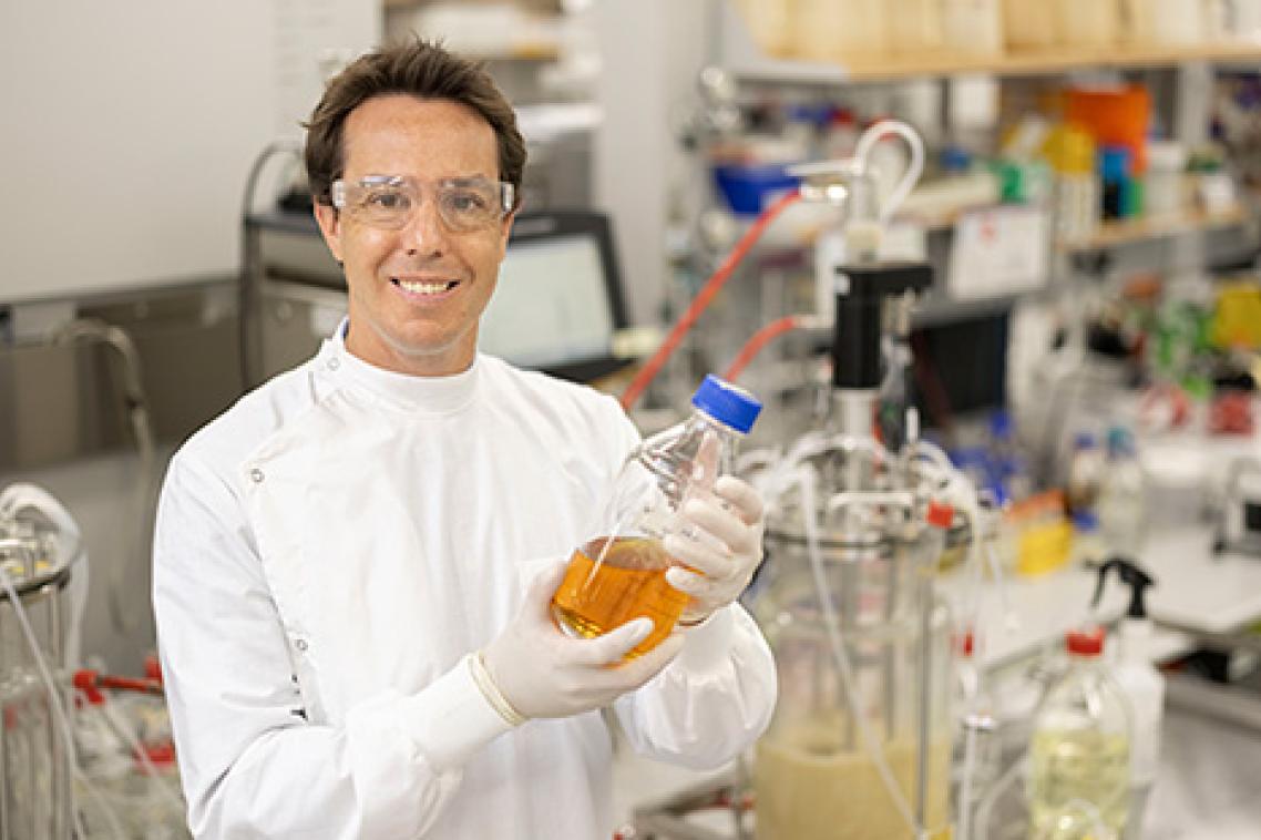 Associate Professor Tim Mercer wearing a lab coat and safety goggles holding a bottle containing orange liquid