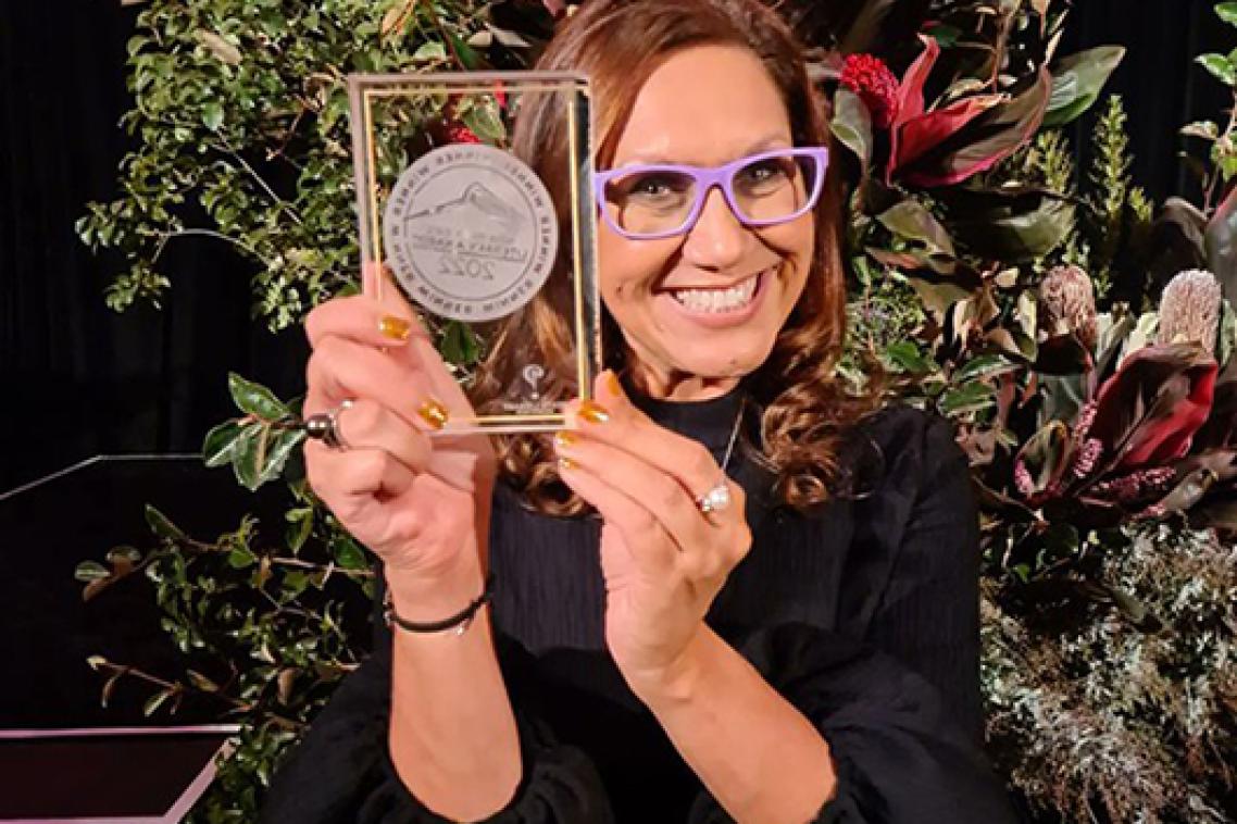 Professor Anita Heiss holding a trophy and smiling