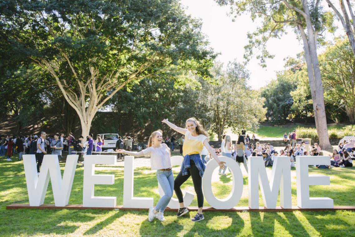 Students at UQ in front of a Welcome sign.