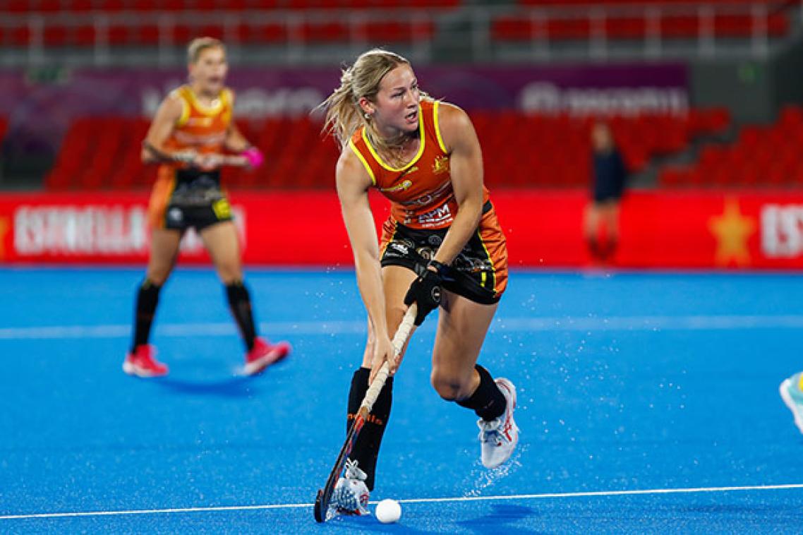 A young hockey player guiding the ball with her stick on a blue hockey field