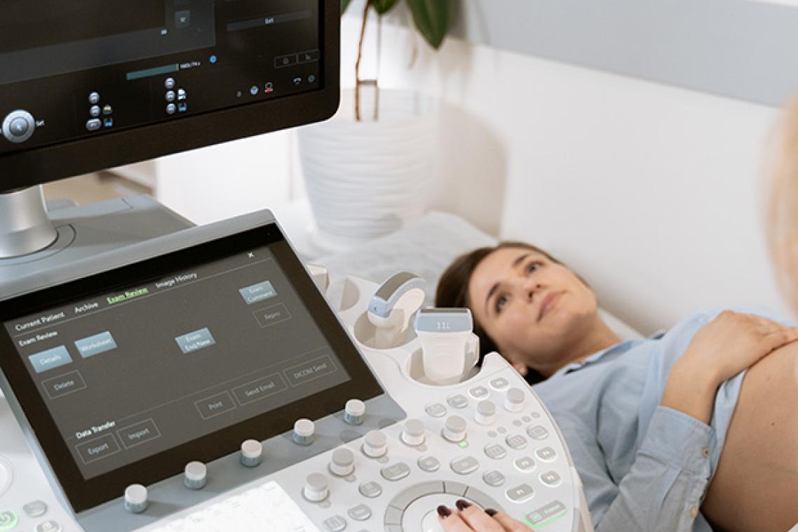 A woman lying on a bed undergoing a sonogram with a concerned look on her face