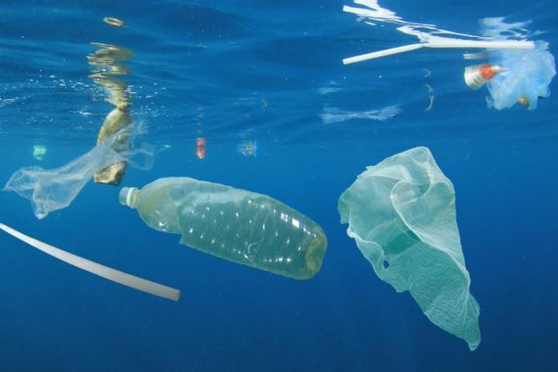 a bottle, plastic bag and straw float in blue water