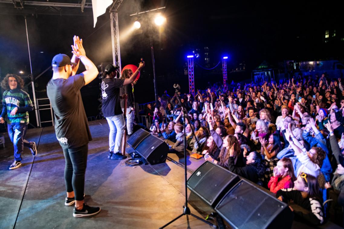 Band playing on stage with crowd in the background.