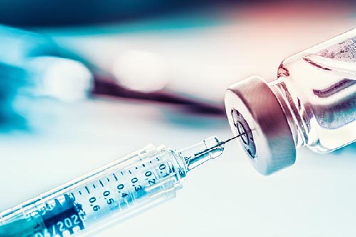 Syringe needle tip going into container of vaccine with blurred background