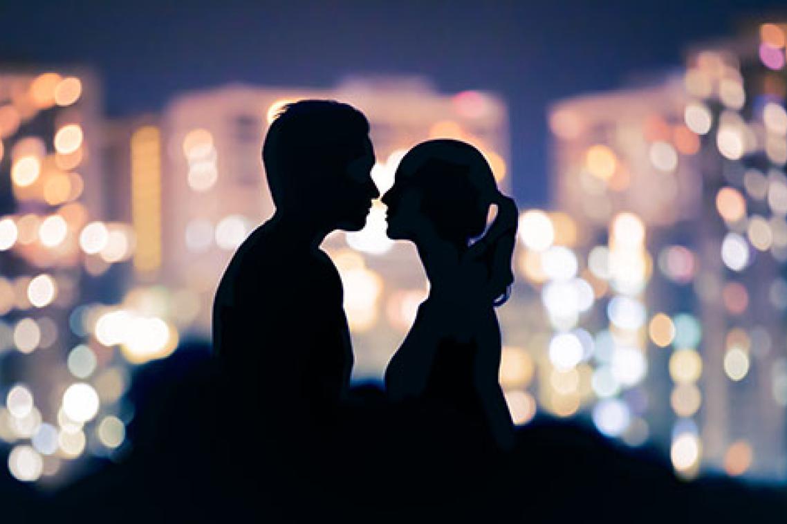 A man and woman in silhoette facing each other with coloured lights behind