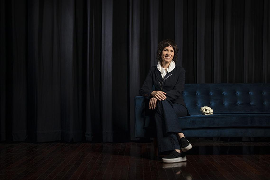 Picture of Deborah Riley sitting right of screen with black curtain behind her