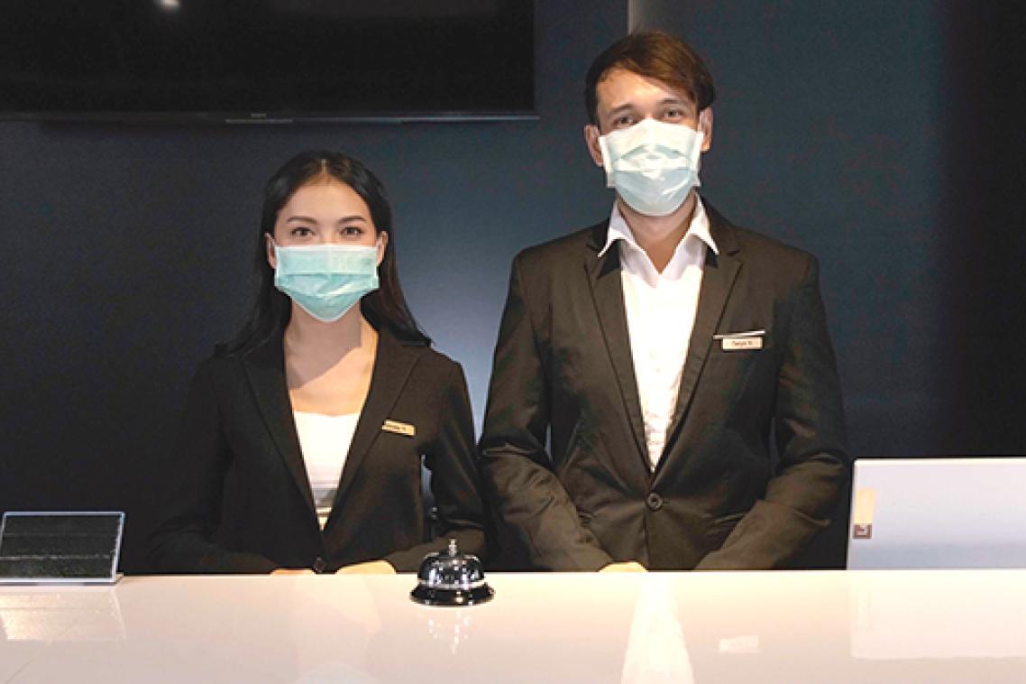 A woman and a man wearing dark suits standing behind a counter in masks