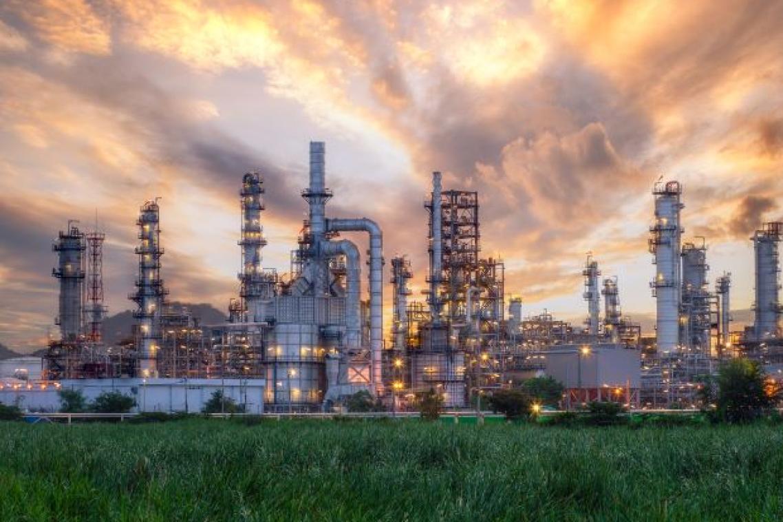 view of a large industrial complex with metal chimneys and scaffolding against a sunset sky