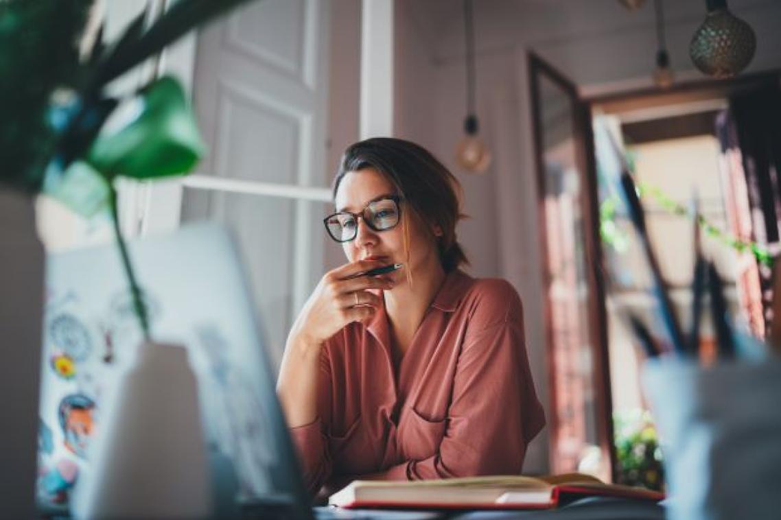 A woman in glasses sits at a desk in a home office looking worried.