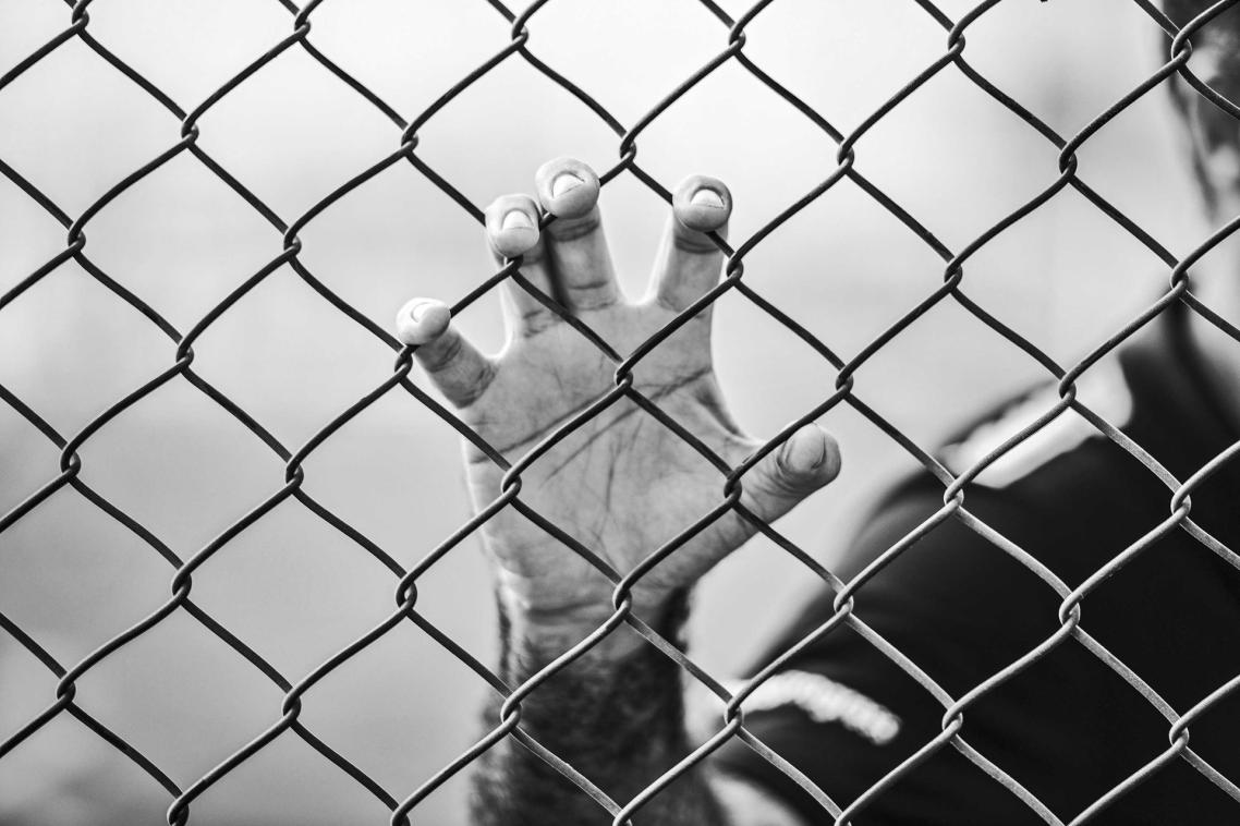 Man's hand grasping a wire prison fence