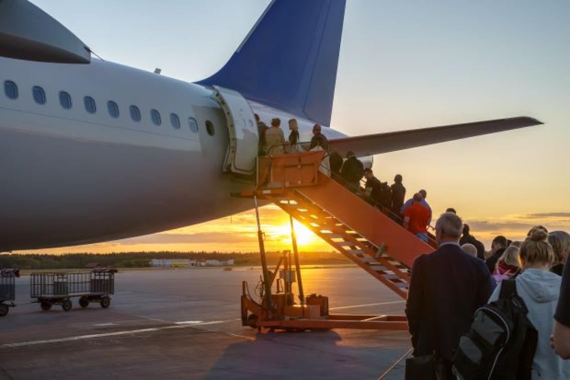 A photo of passengers filing onto a plane parked on airport tarmac at sunset.